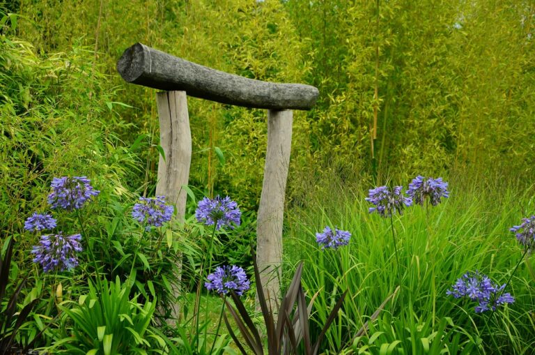 A rustic wooden chair surrounded by lush greenery and blooming purple agapanthus flowers in a garden setting.