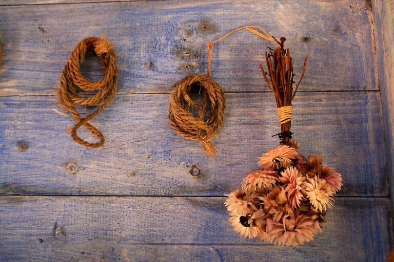 Alt text: Three ropes in varying loops and a bunch of dried flowers with twig bindings hung against a blue wooden background.