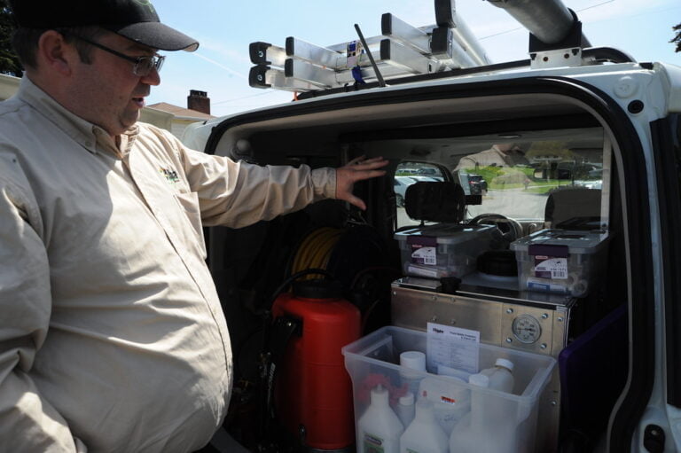 A man in a work uniform opens the back of a van equipped with various technical equipment and containers.