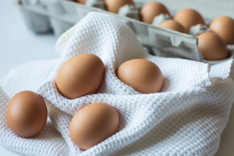 Brown eggs on a white textured cloth beside an open egg carton.