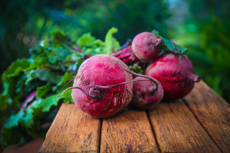 Fresh beetroots with leaves on a wooden surface with a blurred green background.