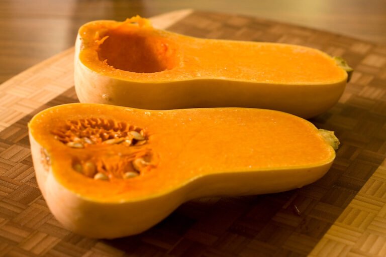 A halved butternut squash on a wooden cutting board, with one half showing seeds and the other hollowed out.