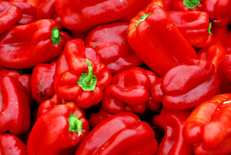 A close-up of a pile of glossy red bell peppers with green stems.