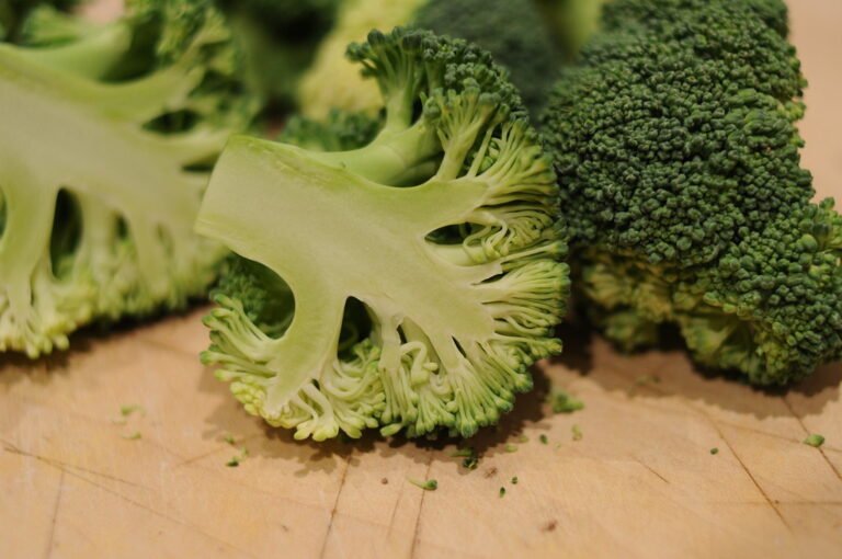 Fresh broccoli florets with stalks on a wooden cutting board.