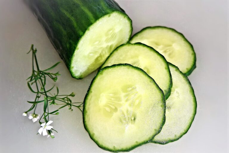 Sliced cucumber with four circular pieces in ascending order next to an uncut portion, decorated with small white flowers and green sprigs on a light background.